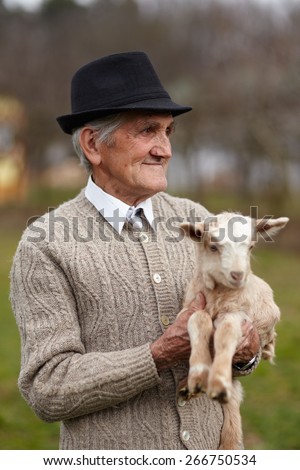 Closeup of a senior man holding a cute baby goat outdoor