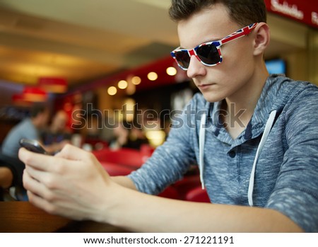 Teenager boy with sunglasses sitting in a restaurant and playing on a smartphone