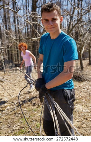 Teenager boy and his mother spring cleaning the orchard, gathering cut branches to throw them away