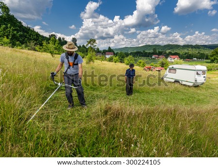 Young farmer mowing the lawn with a trimmer