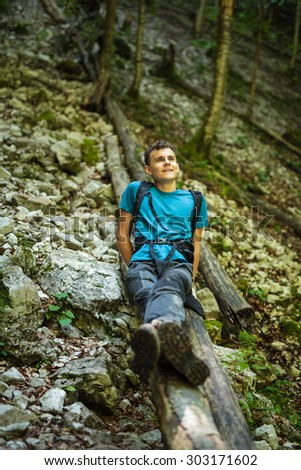 Happy teenager sitting on a log, resting after hiking on a forest trail
