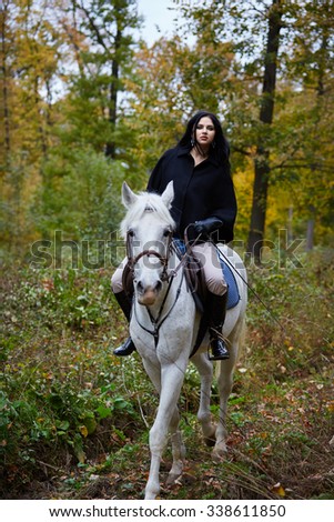 Beautiful young woman riding an white horse in the forest
