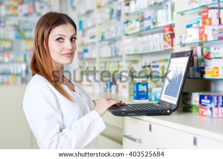 Pharmacist checking stock values on her laptop in the pharmacy near shelves