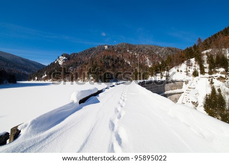 Landscape with foot tracks on a dam frozen lake in the mountains