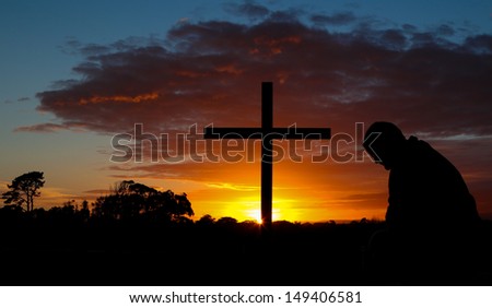 Man in pray before a cross at sunrise.