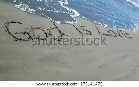 God is Love written in sand as the waves wash close to it.