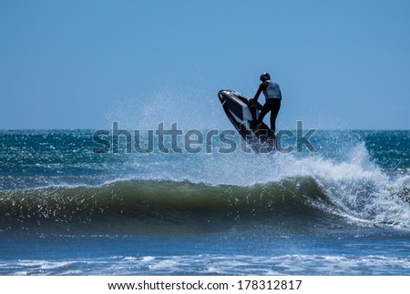 Jet ski flying over a ocean wave on a clear blue sea.