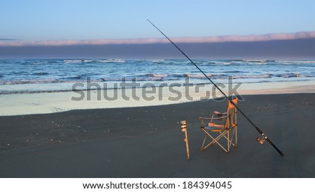 A surf-caster rod and a fishing chair on a beach.