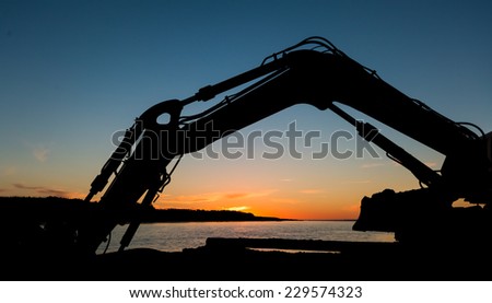 Digger arm stretch out over a sunset by a river mouth area.