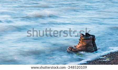 Pair of work boots in water on a beach.