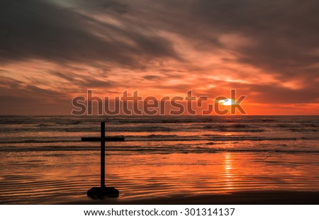 One dark cross on a beach with a wonderful sunset.