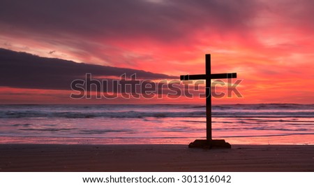 One dark cross on a beach with a wonderful sunset of fire in the sky.