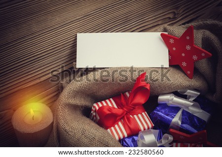Closeup photograph of christmas sack full of gifs. There is an empty card for the xmas greeting message.