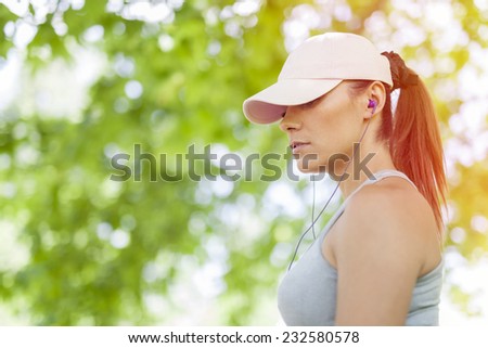 Young female with ear-buds listening to music during sports activity in the park.