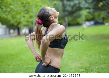young fit woman suffers from back pain during outdoor exercise. Feeling pain in her back.  Sports injury concept.