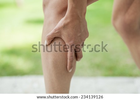 Woman holding sore leg muscle while jogging. Cramp in leg calves. Sports injury concept.