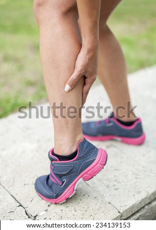 Woman holding sore leg muscle while jogging. Cramp in leg calves. Sports injury concept.