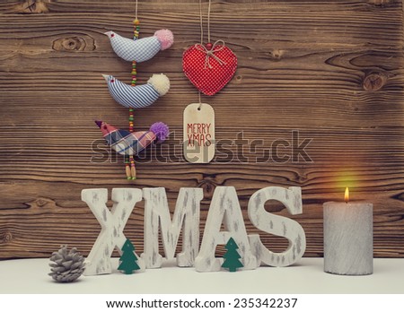 christmas decoration with xmas letters, birds, heart, pine cone, candle and greeting message in front of wood background.