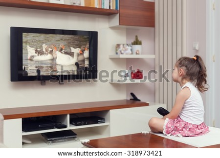 cute little girl having remote control and watching tv