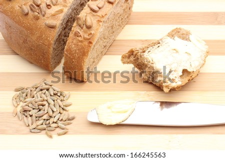 Rye grain, butter on knife and bitten slice of bread lying on wooden cutting board