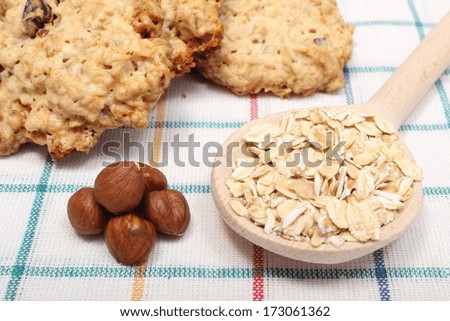Oatmeal cookies and ingredients - oatmeal on wooden spoon and hazelnut lying on colored background