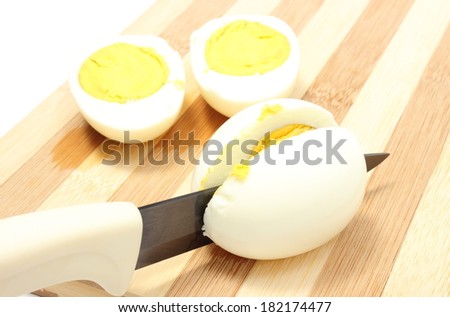 Halves of eggs with ceramic knife, sliced egg with knife on wooden cutting board