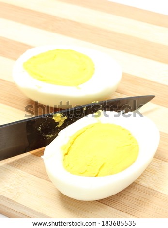 Two halves of egg with ceramic knife, sliced egg with knife on wooden cutting board