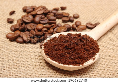 Ground coffee on wooden scoop and coffee beans in background, coffee grains. Background texture of old jute