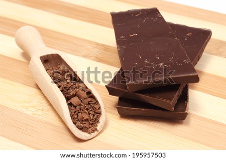 Grated chocolate on wooden spoon and stack of dark chocolate, chocolate pieces. Isolated on wooden background