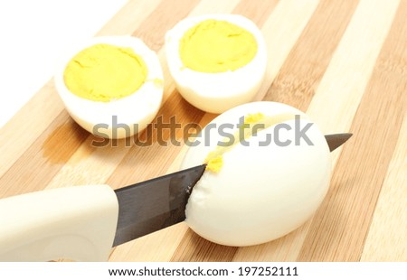 Halves of eggs with ceramic knife, sliced egg with knife on wooden cutting board