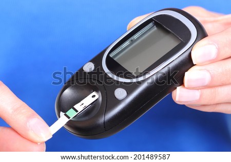 Closeup of strip for glucose testing and glucose meter, measuring sugar level. Isolated on blue background