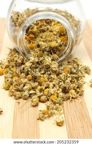 Closeup of dried chamomile, dried chamomile pouring out of glass jar on wooden cutting board