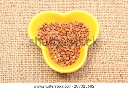 Closeup of buckwheat groats in yellow bowl lying on jute canvas, healthy food and healthy nutrition