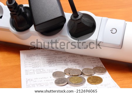 Electrical plugs with cords connected to electrical power strip with On-Off switch, electricity bill with heap of coins, concept of energy saving