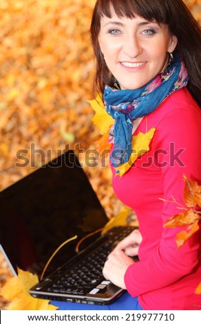 Smiling woman writing on a laptop in autumn park