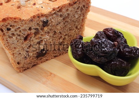 Fresh baked wholemeal bread and heap of dried plums lying on cutting board, concept for healthy eating