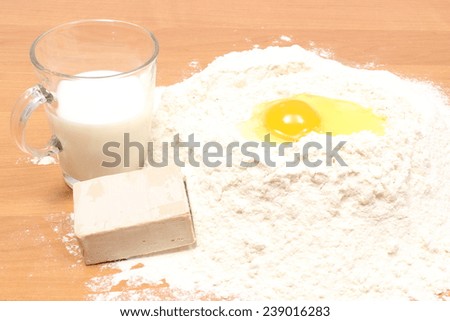Heap of wheat flour, glass of milk, egg and cube of yeast lying on wooden table, baking ingredients, preparing yeast cake