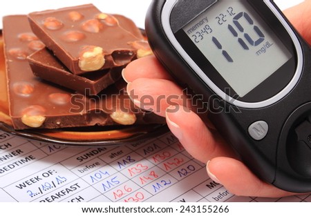 Hand of woman with glucose meter and portion of chocolate on medical form with results of measurement of sugar, concept of measuring sugar level