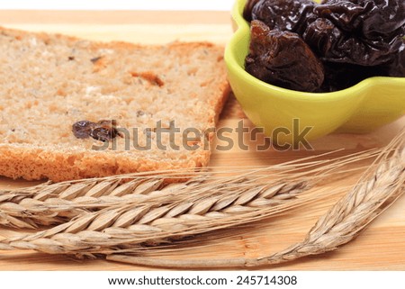 Fresh baked wholemeal bread, heap of dried plums and ears of wheat lying on cutting board, concept for healthy eating