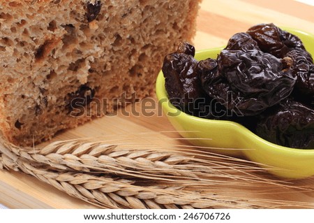 Fresh baked wholemeal bread, heap of dried plums and ears of wheat lying on cutting board, concept for healthy eating