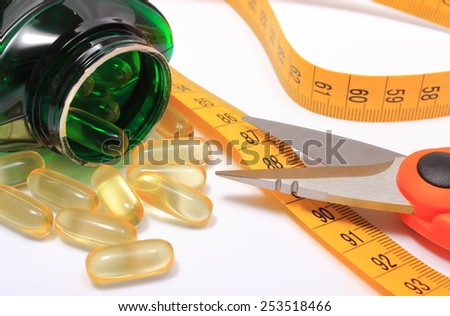 Orange scissors with tape measure and slimming pills poured from bottle on white background, concept for slimming