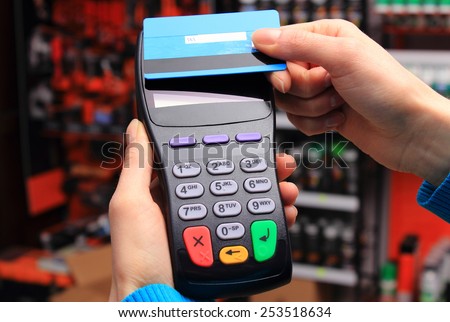 Hand of woman paying with contactless credit card with NFC technology in an electrical shop, credit card reader, payment terminal, finance concept