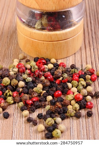 Heap of fresh colored pepper with pepper mill lying on wooden table, seasoning for cooking, concept for healthy nutrition