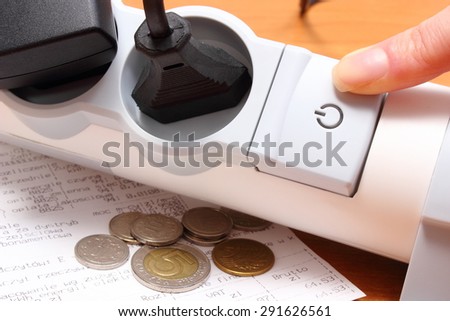 Finger of woman turns off electrical extension, electrical plugs connected to electrical power strip, electricity bill with coins, concept for energy saving