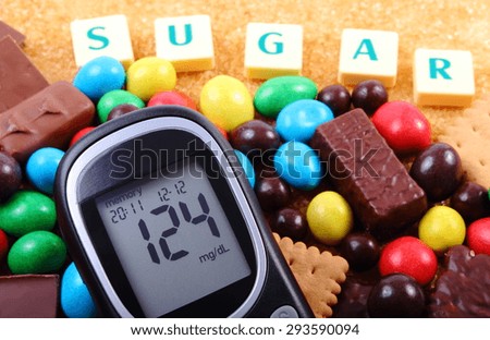 Glucose meter with word sugar, heap of candies, cookies and brown cane sugar, too many sweets, unhealthy food, concept of diabetes and reduction of eating sweets