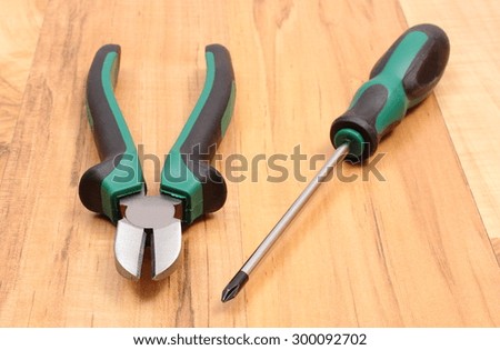 Metal pliers and electrical screwdriver on wooden surface, work tools and accessories for engineering jobs
