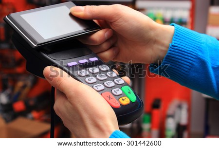 Hand of woman paying with NFC technology on mobile phone in an electrical shop, credit card reader, payment terminal, finance concept
