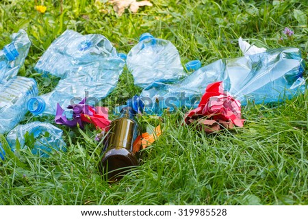 Heap of rubbish on grass in sunny park, plastic and glass bottles, bottle caps and paper, concept of environmental protection, littering of environment