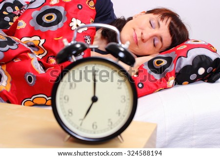 Beautiful woman sleeping on bed in her bedroom and ringing alarm clock