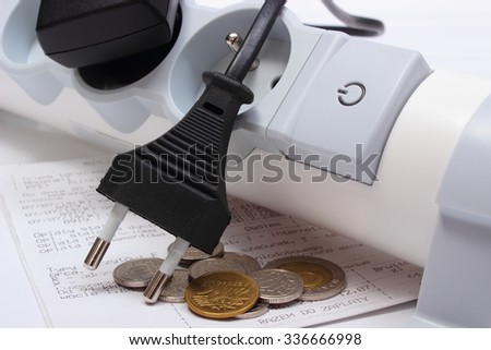 Electrical plugs with cords disconnected from electrical power strip, electricity bill with heap of coins, concept of energy saving